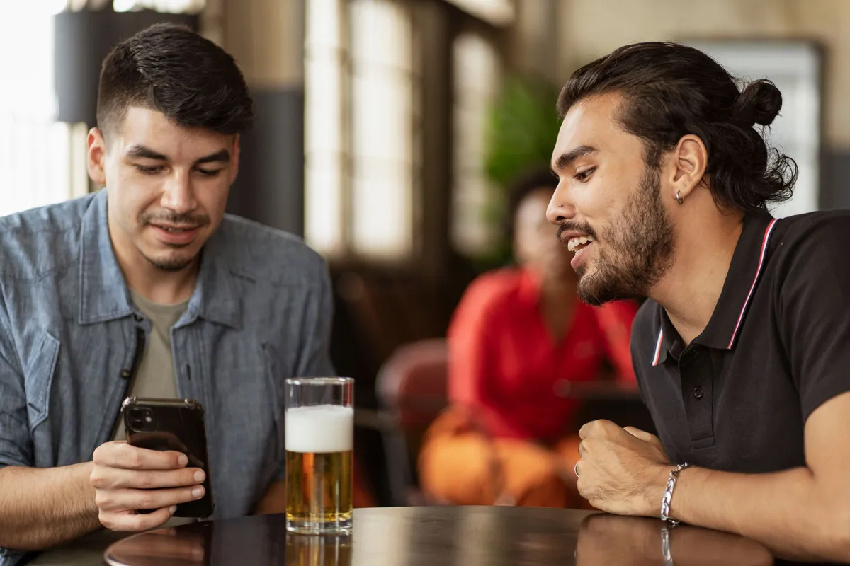 Two friends at a pub table, one of them checking a plan on his phone