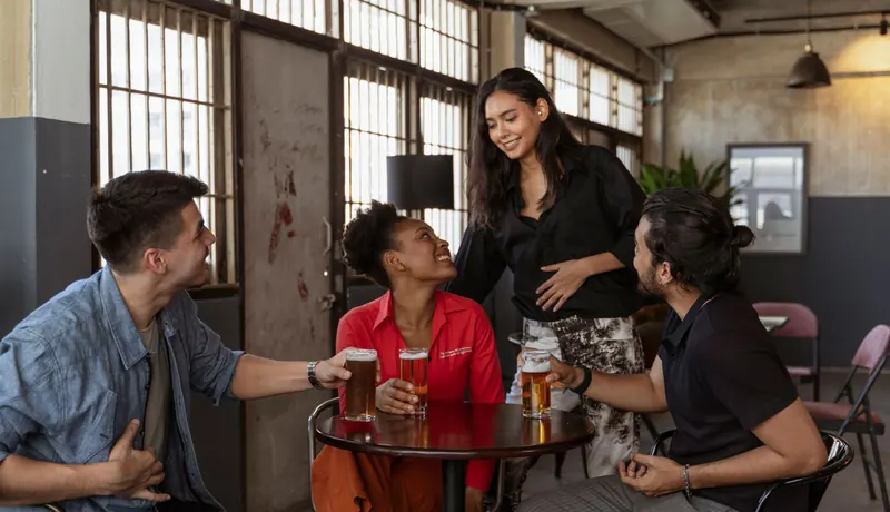A group of friends laughing over beers at a table in an industrial bar
