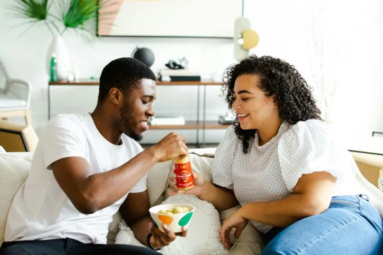 A couple sitting on a sofa sharing a bowl of snacks and laughing