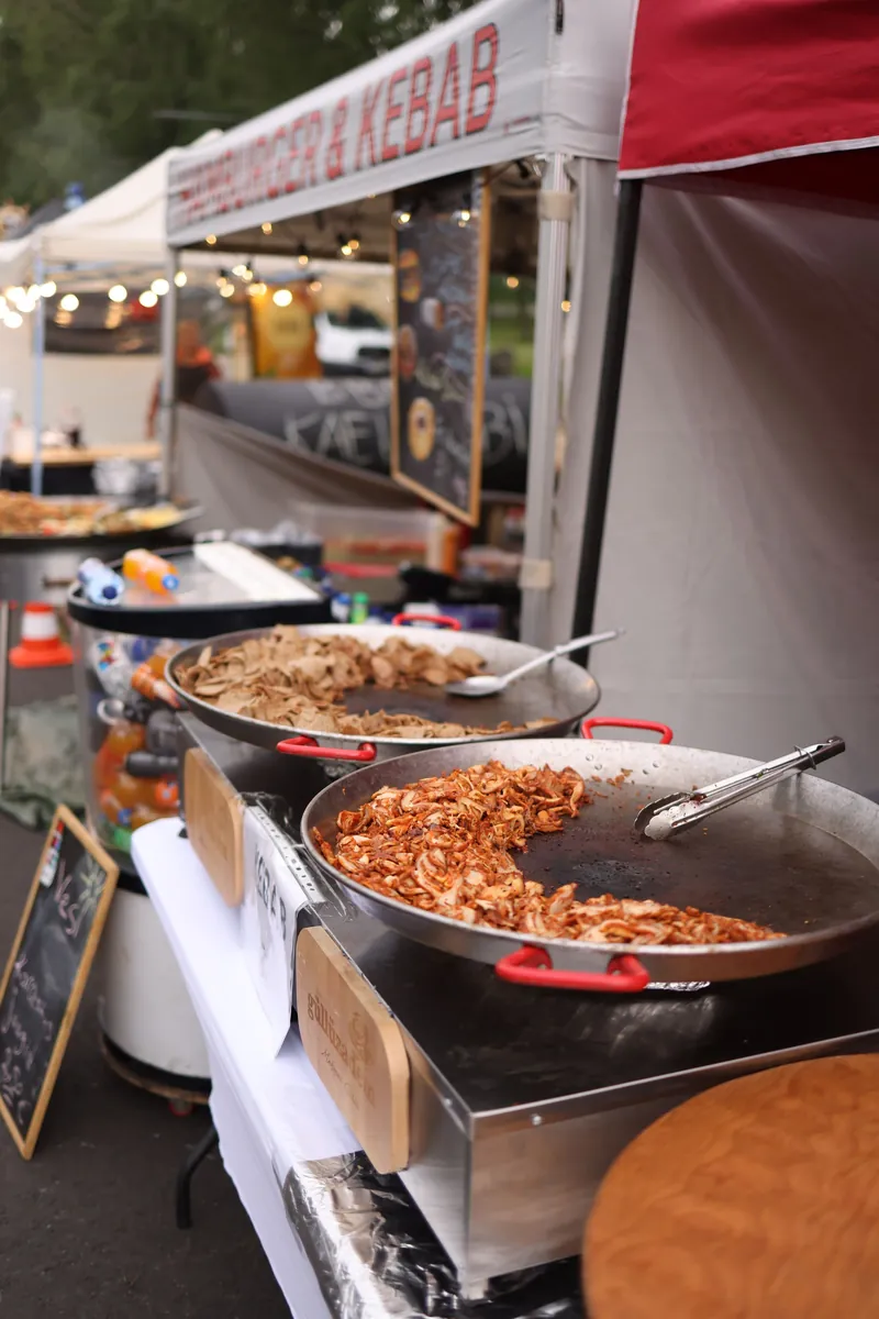 Food stalls at an open-air market, large pans of noodles and rice under hanging lights