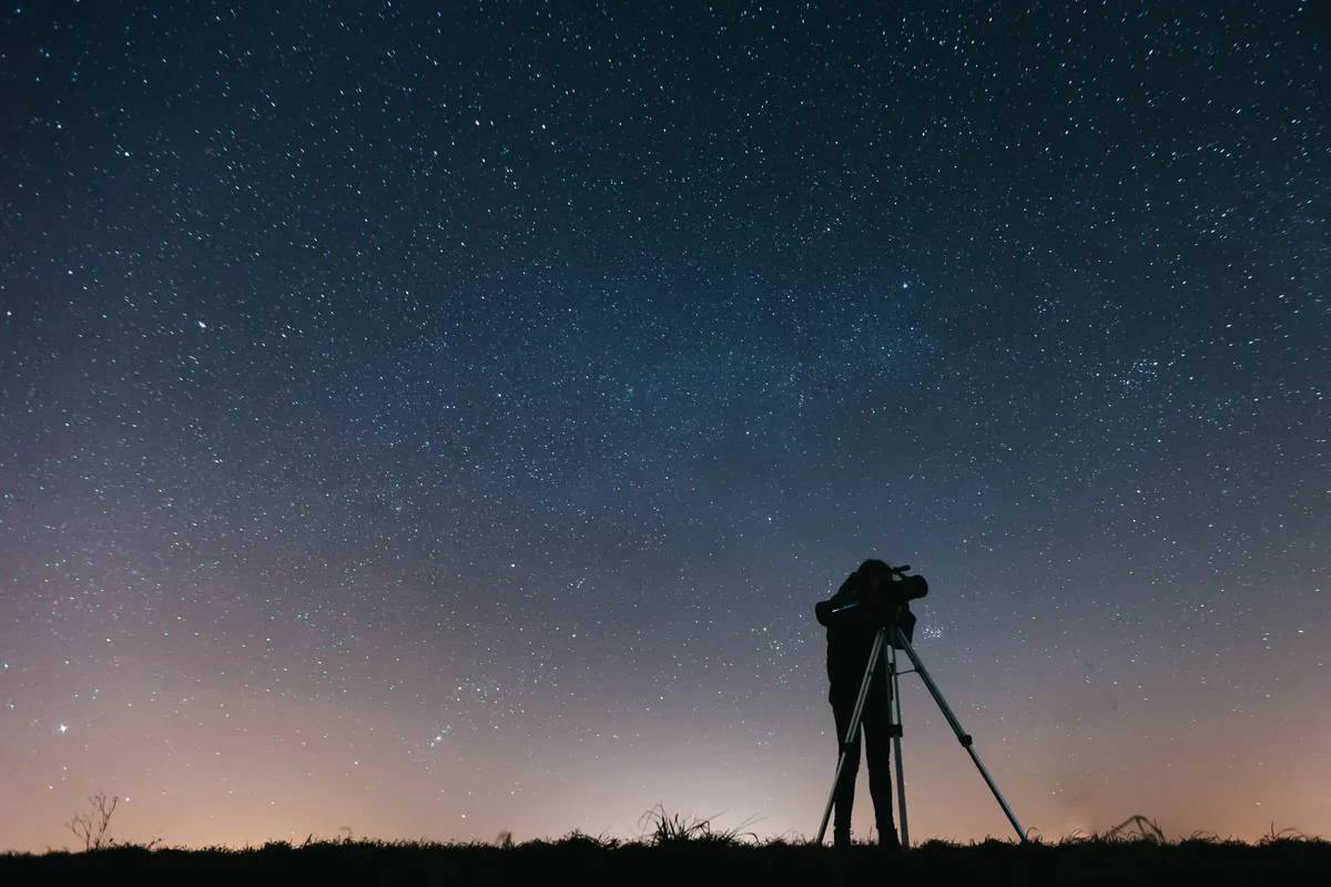 A telescope silhouetted against a star-filled night sky, a figure standing beside it