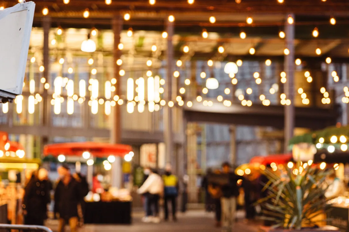 An evening market hall strung with warm lights, people moving between stalls