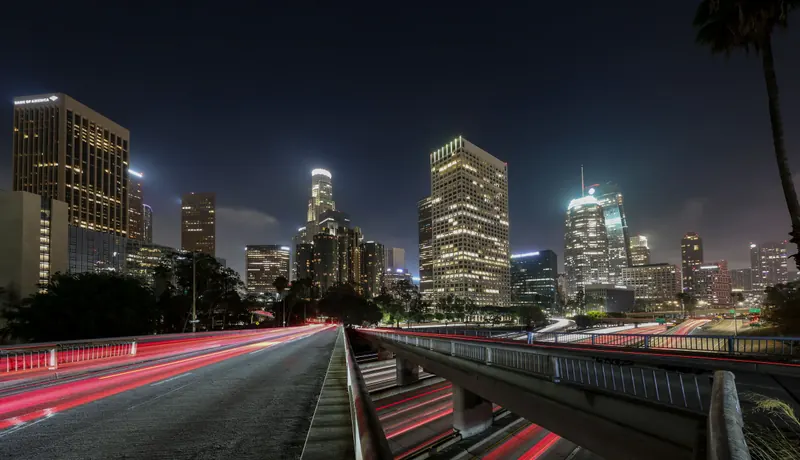 Downtown Los Angeles skyline at night with light trails on the freeway below