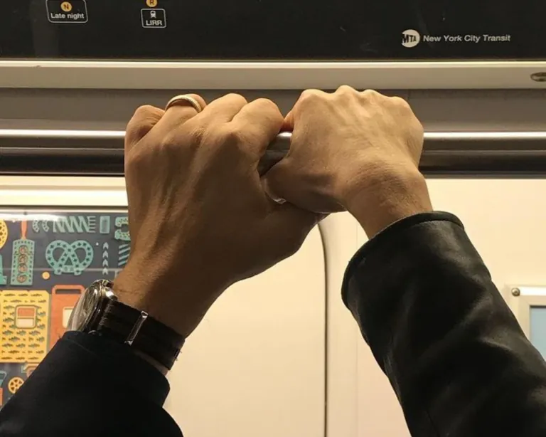 Two hands gripping the same pole on a New York City subway train