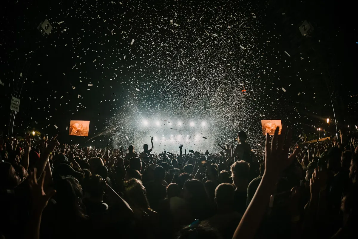 A packed crowd at an outdoor show at night, hands in the air under stage lights