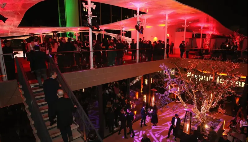 An open-air Los Angeles venue at night, crowds spread across two levels under red light