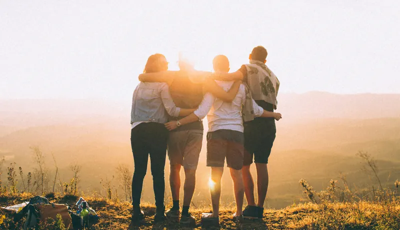 Four friends standing arm in arm on a hilltop at sunset