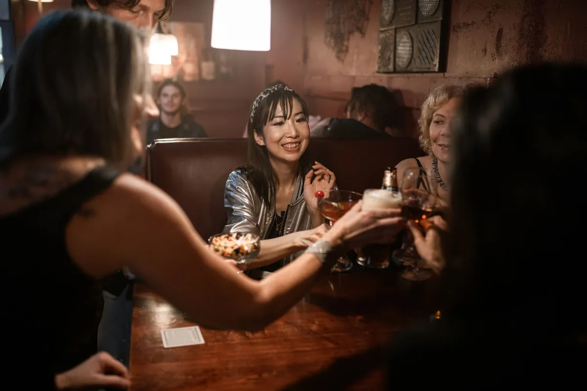 A group of friends laughing and clinking glasses around a bar table at night