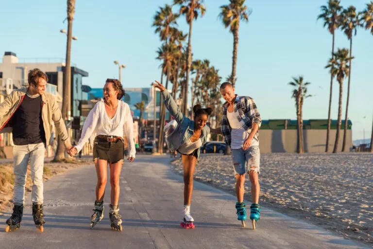 Four friends rollerblading along a palm-lined path by the beach