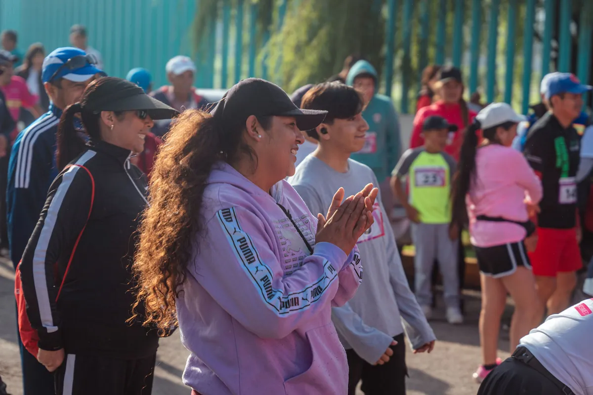 A crowd of runners in caps and hoodies clapping and laughing at the start of a community fun run on a sunny morning