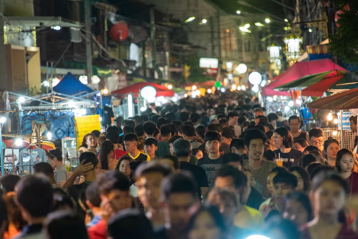 A packed night market, lanterns strung overhead, crowds moving between the food stalls