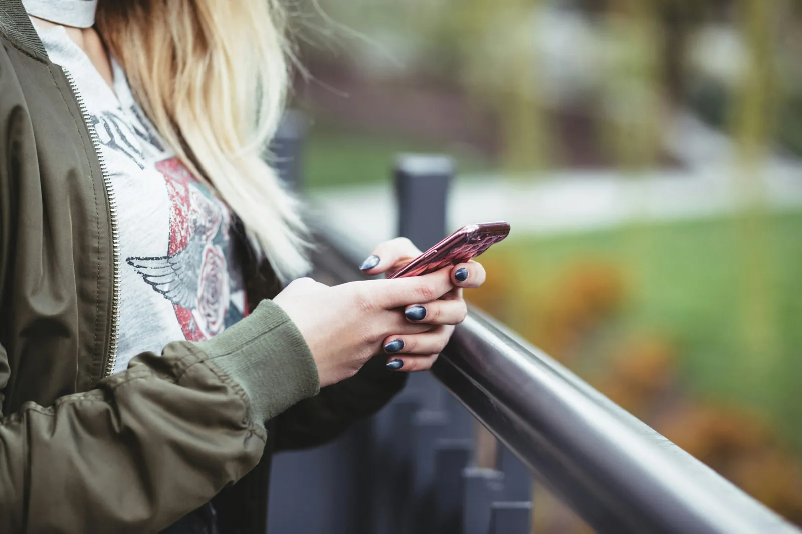 A person leaning on a railing outdoors, typing a message on their phone