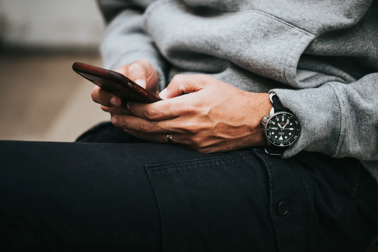 A person sitting down, holding their phone in both hands mid-message