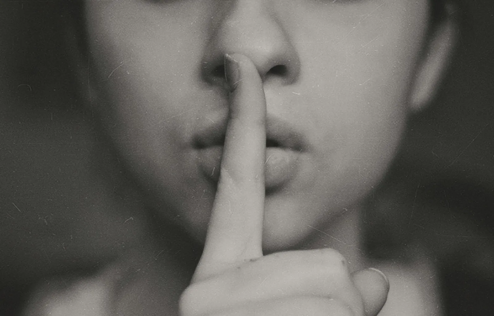 A black and white close-up of a woman holding one finger to her lips