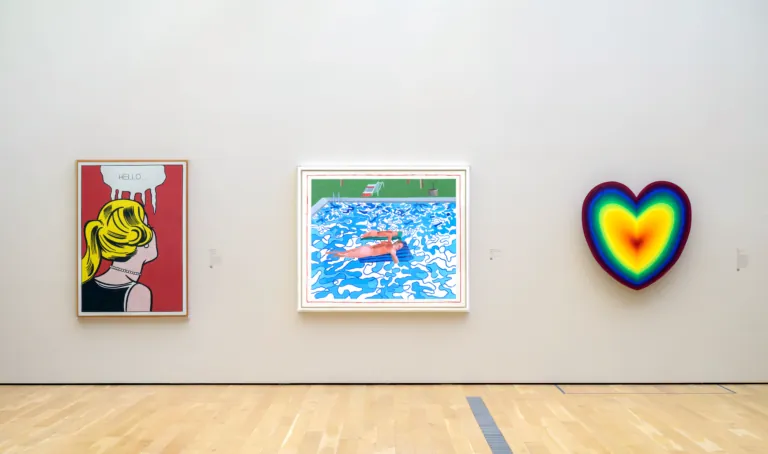 Three works on a gallery wall at LACMA: a comic-style panel, a swimming pool painting, and a rainbow neon heart