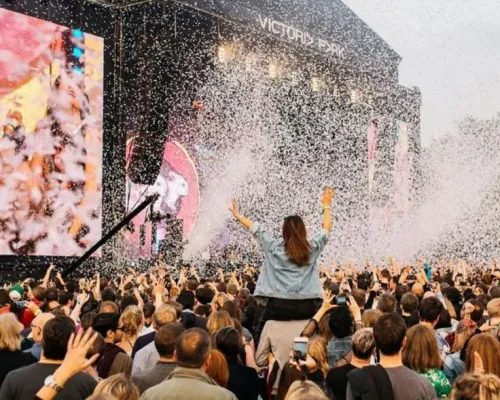 A performer facing a packed festival crowd as confetti falls across the stage