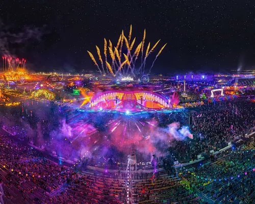 An aerial view of a festival main stage at night, lit up with fireworks overhead
